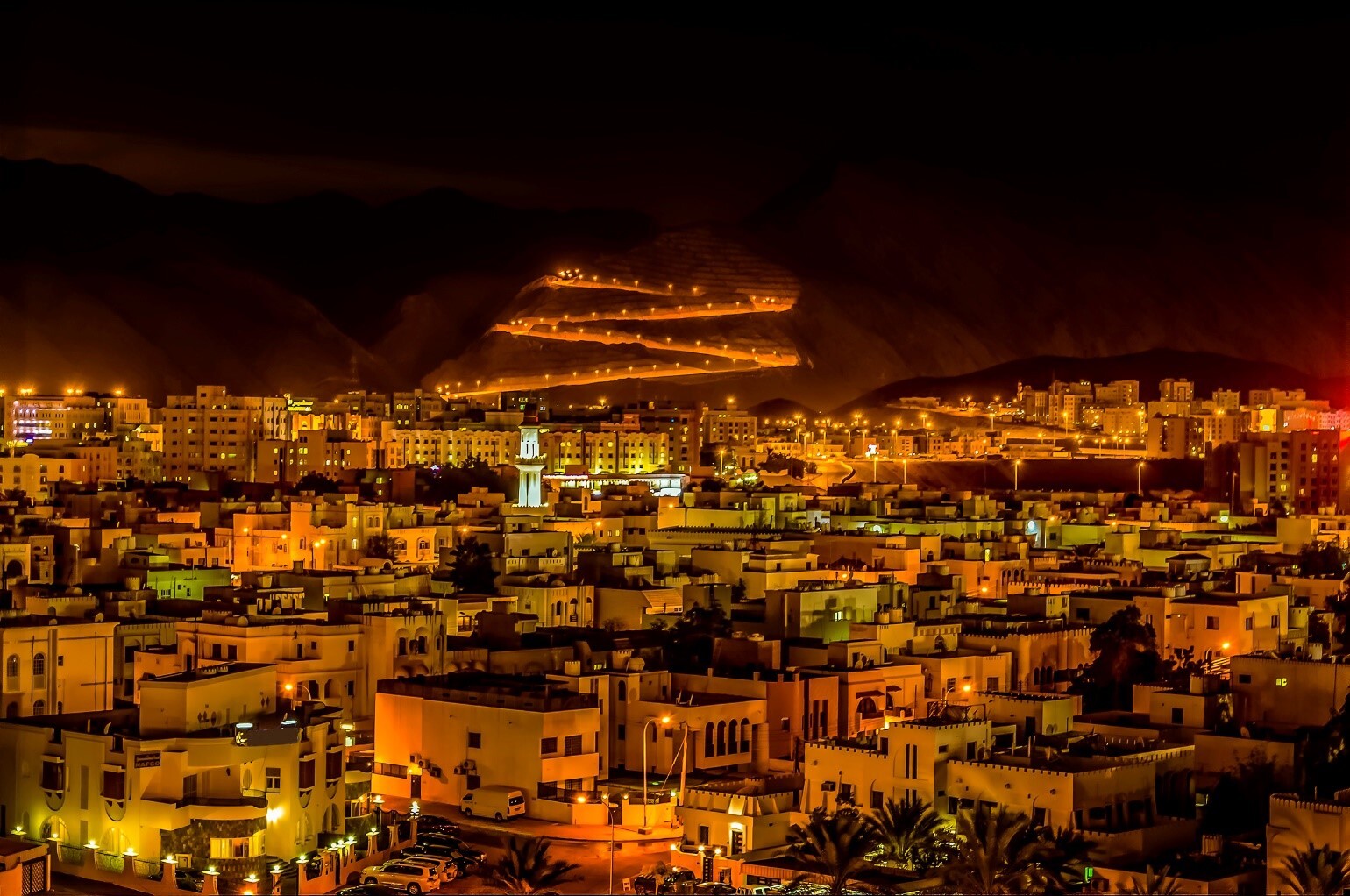 Night view of Muscat, Oman, with glowing terraced mountain roads and city lights, highlighting the region where Gradiant enhances industrial water and wastewater operations via MPES acquisition.
