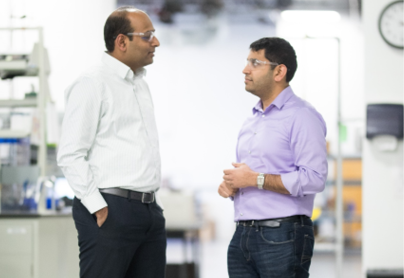 Prakash and Anurag in conversation at a Gradiant lab, wearing safety glasses and business casual attire, reflecting teamwork and technological progress in water treatment innovation.
